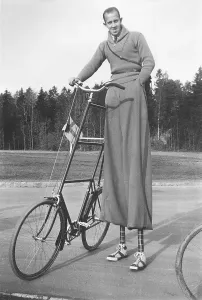 Odd bicycle with equally odd cyclist in the 1940s. A man seen on stilts to be able to ride his taller than usual bicycle. His equally long trousers covers the stilts and they are in the typical 1940s design breeches plus fours