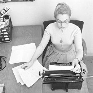 Office girl in the 1950s. A woman is sitting at a office desk typing on her typewriter. 1957