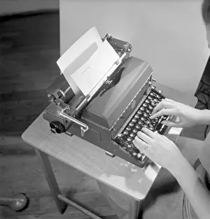 Office girl in the 1950s. A woman is sitting at a office desk typing on her typewriter
