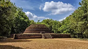 An old brick stupa surrounded by thick greenery and a cloudy sky