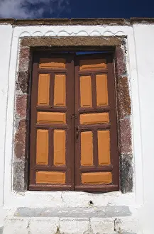 Old brown and orange painted wooden entrance doors on exterior of white roughcast cladded residential building