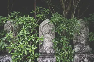 Three old buddhist statues covered in green leaves at Daisho-in temple in Miyajima