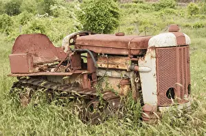 Old neglected rusty small vintage caterpillar tractor on green meadow