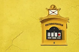 An old nostalgic post box hangs on a yellow house facade