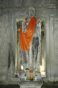 Old statue of a standing Buddha wearing an orange cape