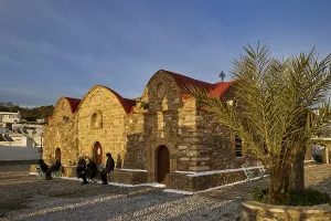 An old stone building with a red roof next to a palm tree in the soft evening light