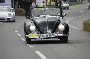 An old Volkswagen Beetle convertible drives past spectators at a car race