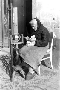 An old woman weaves on the street, ca