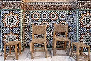 Old wooden chairs and stools in front of a beautiful tiled wall
