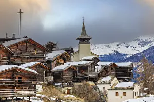 Old wooden houses with snow-covered roofs and the Saint Theodule church in the historic village centre