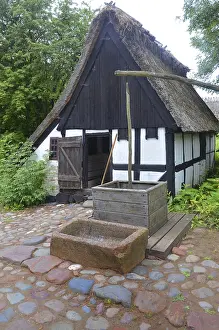 Older half-timbered house with thatched roof by older well in Den gamle by