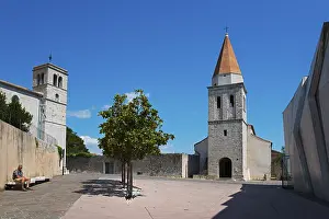 Open square with two church towers and trees under a clear sky