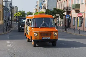 Orange bus drives through a sunny city street