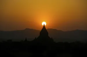 Orange sunset, silhouette with the sun behind the steeple of a Buddhist temple