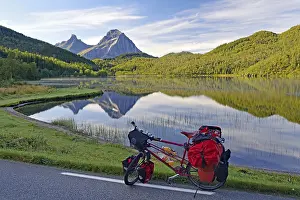 Packed touring bike in front of mountain lake and steep mountains