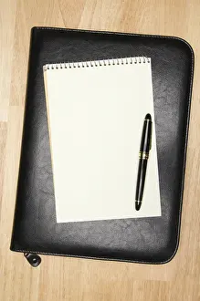 Pad of paper, pen & leather binder on a wooden background<br> Pad of paper