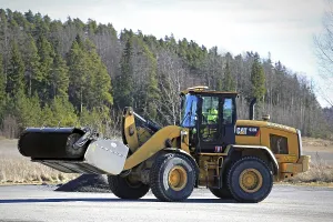 PAIMIO, FINLAND, MARCH 18, 2017: CAT 938K wheel loader and bucket sweeper at work to clean an asphalt yard at spring