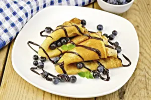Two pancakes with blueberries, mint and chocolate icing on a plate