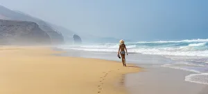 Panoramic of a young tourist with a hat walking alone on the Cofete beach of the Jandia natural park