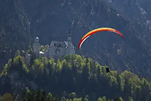 A paraglider glides over Neuschwanstein Castle against a mountainous backdrop