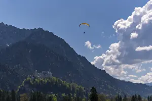 A paraglider over Neuschwanstein Castle with a cloudy sky