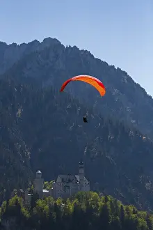 Paraglider over Neuschwanstein Castle in the middle of a natural mountain landscape