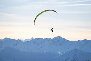 Paragliders flying over snowy mountain peaks in winter in evening light