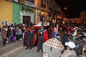 Participants in black and red robes carry a coffin during a night procession