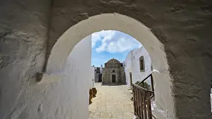 Passage through a stone arch with a view of white buildings and blue sky in the Greek monastery
