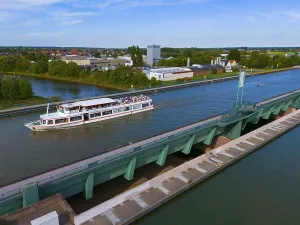 A passenger ship sails on a canal over a large bridge