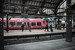 Passengers waiting on a platform beside a red train within a station in Copenhagen
