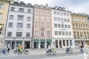 Passers-by ride along on bicycles in front of colourful building facades in Munich
