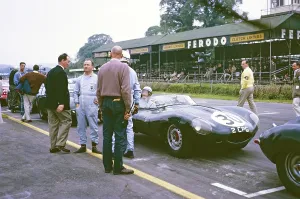 Pat Coundley in the car, John Coundley stands on the driver's side in blue overalls and looks into the camera, Jaguar D Type, Whitsun Sports Car Race in Goodwood, 3 June 1963