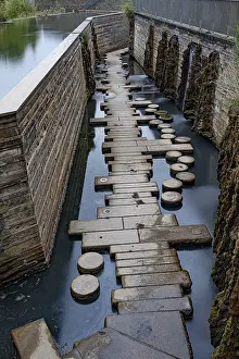 A path of stones leads through a narrow waterway next to a wall