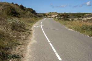 Paved road winds through grassy dunes on a sunny day
