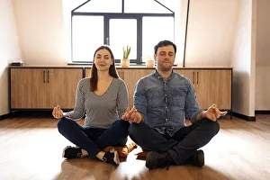 Peaceful adult couple in sportswear sitting on the floor in lotus pose with eyes closed