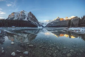 Peaceful lake reflecting snow-capped mountains and a cabin under a clear blue sky at sunrise, Lake Louise, Canadian Rockies