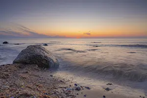 A peaceful sunset by the sea with a large rock in the foreground