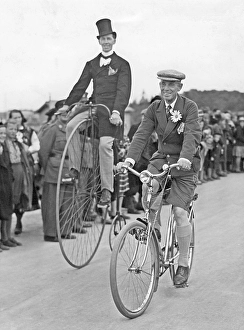 Penny farthing bicycle. A man is riding a penny-farthing bicycle besides a man on a regular bicycle