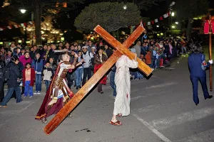 People carrying a large cross while being watched by a crowd in the city at night