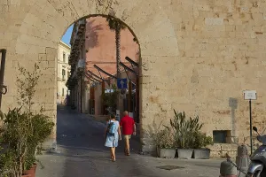People crossing a historic stone city gate surrounded by plants