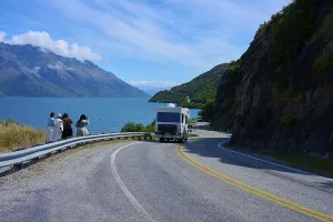 Framed Print : People enjoying travelling and a motorhome on a winding road next to a lake surrounded by mountains