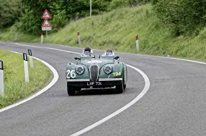 Two people in a green vintage convertible with racing numbers