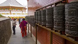 People interact with prayer wheels in a Buddhist-decorated temple with a red and gold accent