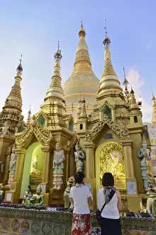 People looking at golden stupas of a temple at sunset