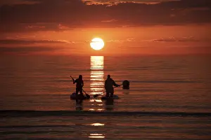 Two people paddling in the calm sea at sunset on stand-up paddle
