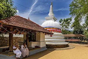 People pray in front of temples and white stupa under a blue sky