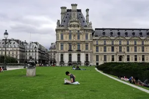 People relaxing on a lawn in front of a historic building in the Louvre complex
