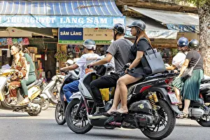 People ride scooters through a busy city shopping street during the day
