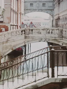 Two people standing on a historic Sighs bridge over a canal on a sunny day